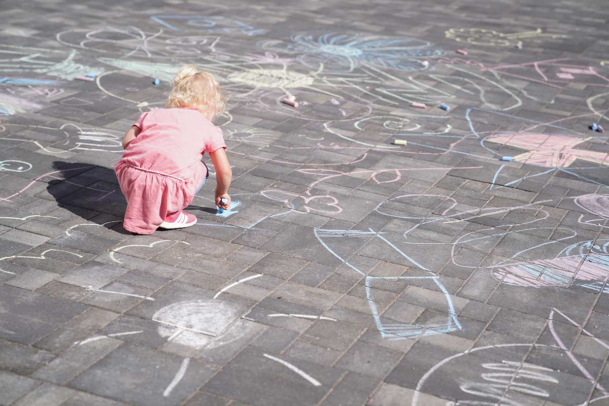 Tochter Martha malt mit Malkreide. Um sie herum sind bereits zahlreiche Kunstwerke auf dem Pflaster zu sehen.